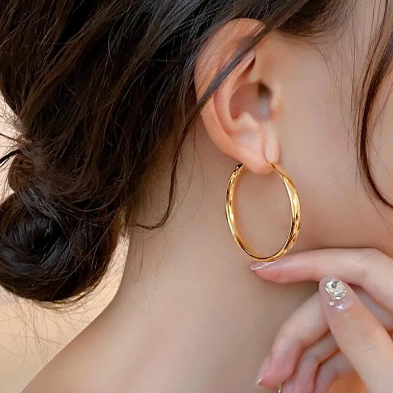 A pair of large, circular gold metal hoop earrings on a flat surface.
