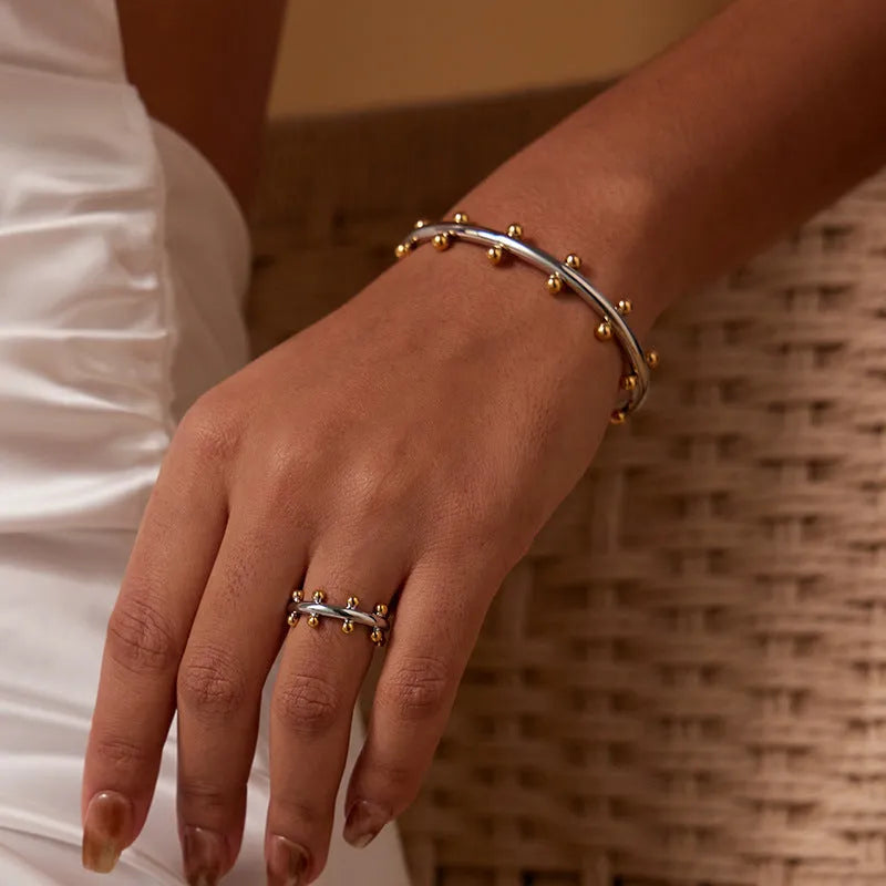 Stainless steel C-shaped bracelet with rivet-shaped bean beads in a steel-gold colour finish.