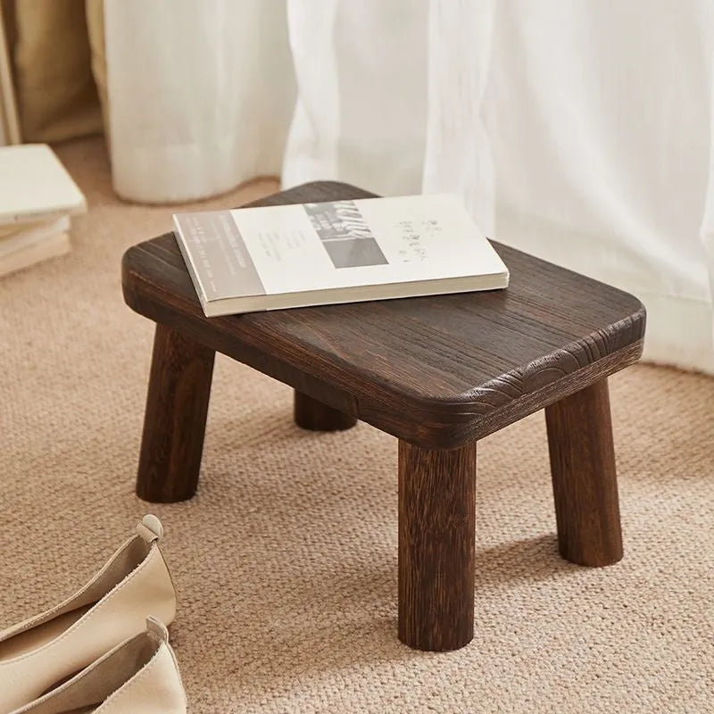 Solid wood distressed finish changing stool with bracket legs on a wooden floor.