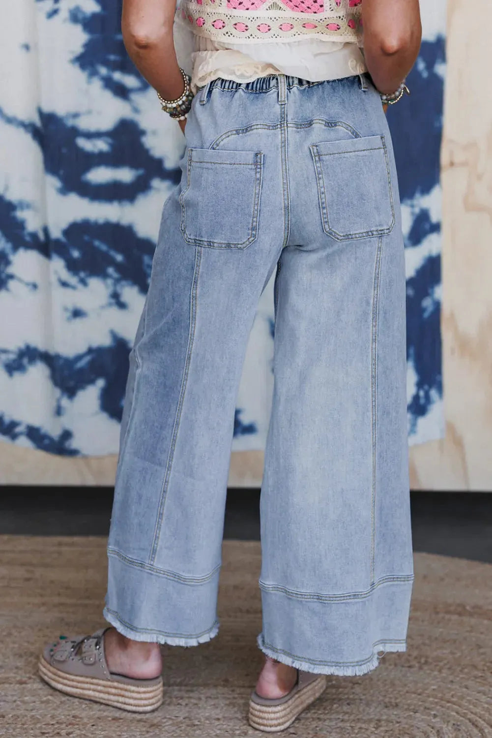 Beau Blue colour wide leg denim trousers with a drawstring waist and raw hem seam detail laid flat.