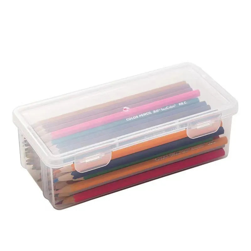 Clear plastic stationery storage box full of coloured pencils and drawing tools on a table.