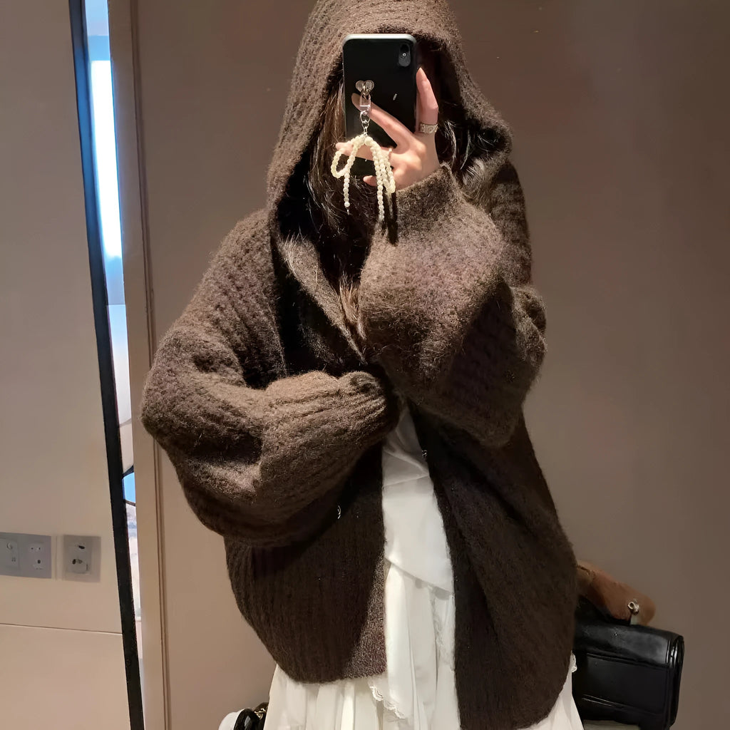A woman wearing a thick, dark grey hooded cardigan with a loose fit and regular sleeves.