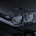 Black head-mounted smart Bluetooth glasses with a transparent lens on a colour box.