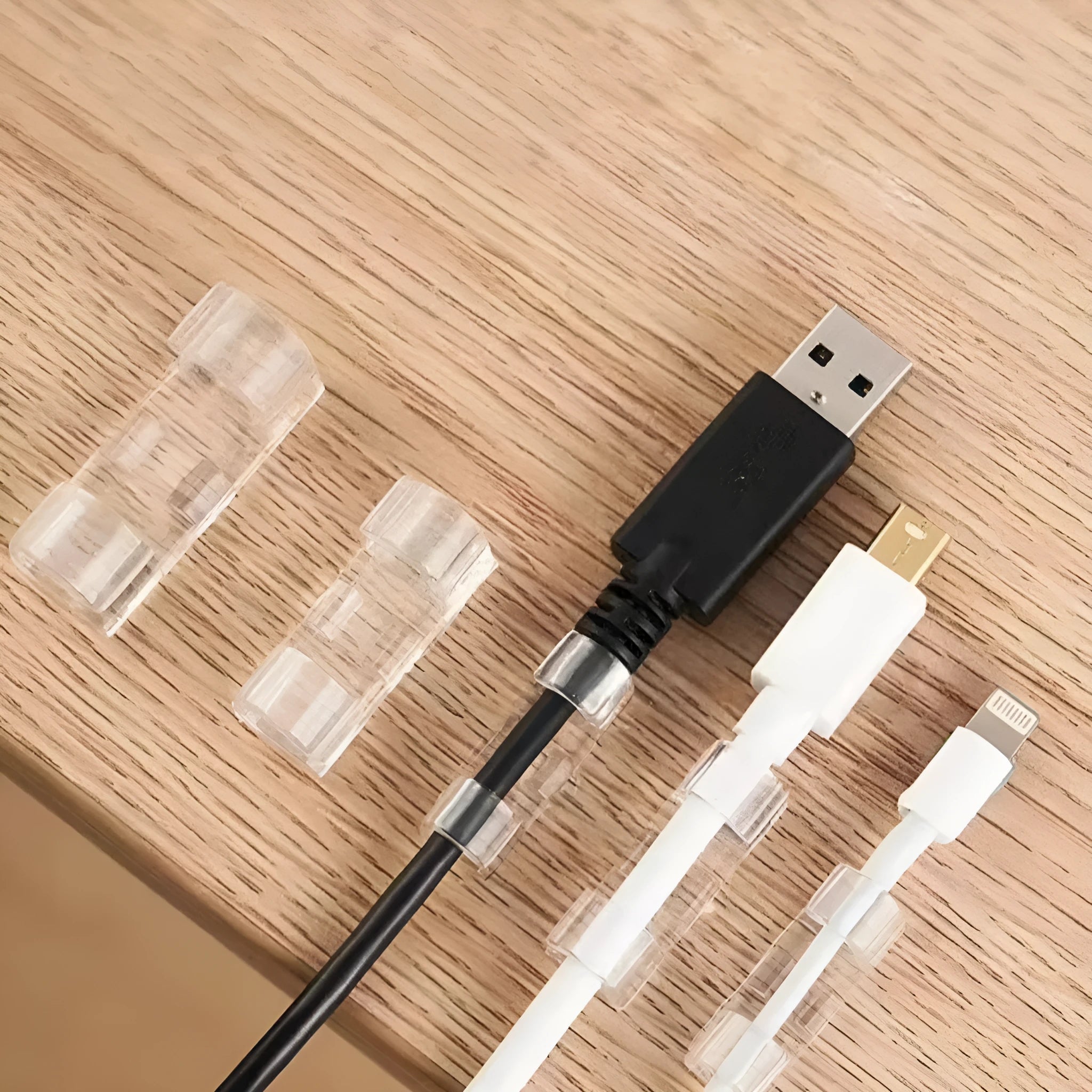 Transparent plastic self-adhesive wire holder routing snap clip on a desk surface with a white cable inserted