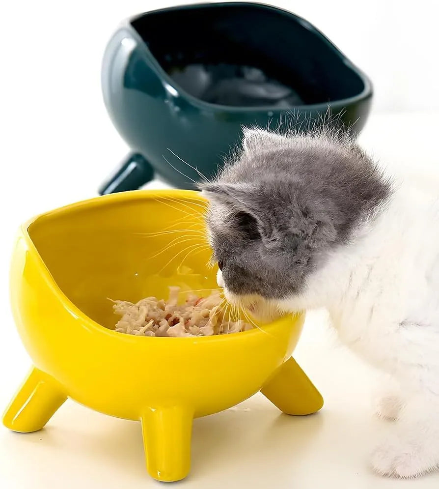 Green ceramic cat food bowl with four legs, wide mouth, and rounded arc shape on a light floor
