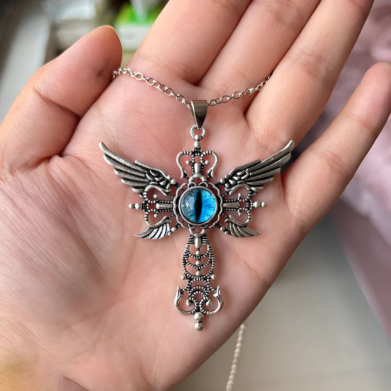 Close-up of a blue alloy necklace featuring a geometric cross pendant with detailed devil wings.