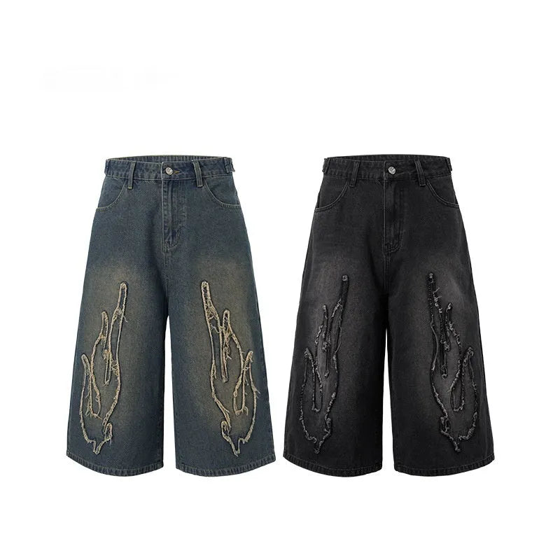 Men's black cropped denim shorts with red and orange patch flame embroidery on the leg.