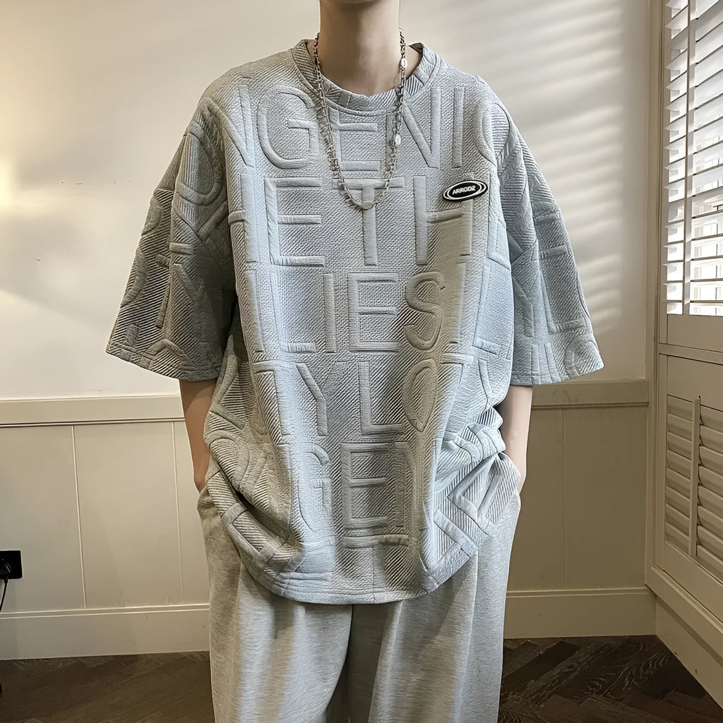 Men's grey loose-fit t-shirt with a raised 3D letter print on the front.