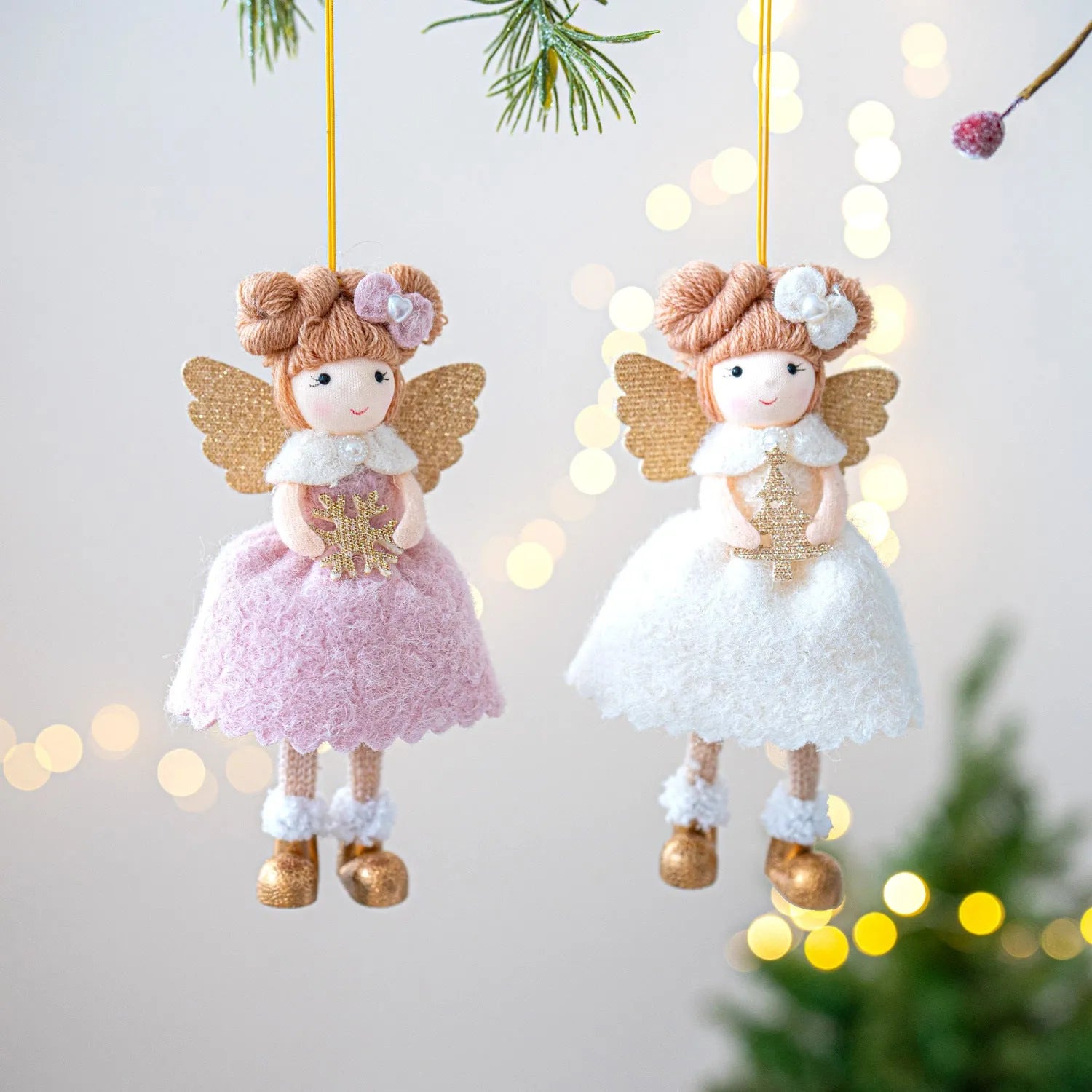 Soft pink cloth Christmas pendant ornament shaped like angel wings on a green branch.