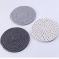 Three round grey cotton cord coasters on a wooden table