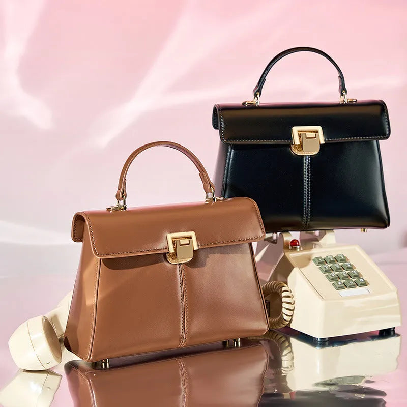 Black leather women's shoulder bag with vachette clasp showing square shape and adjustable strap.