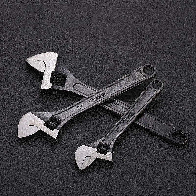 Blackened high carbon steel adjustable open-end wrench on a workbench, jaw set to mid-opening.
