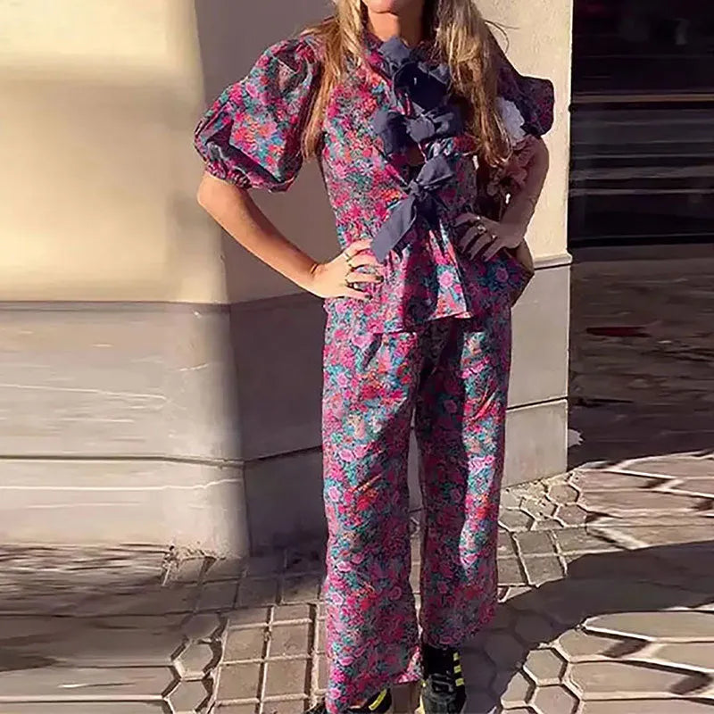 Women's floral print trouser suit with tie-neck blouse featuring puff sleeves