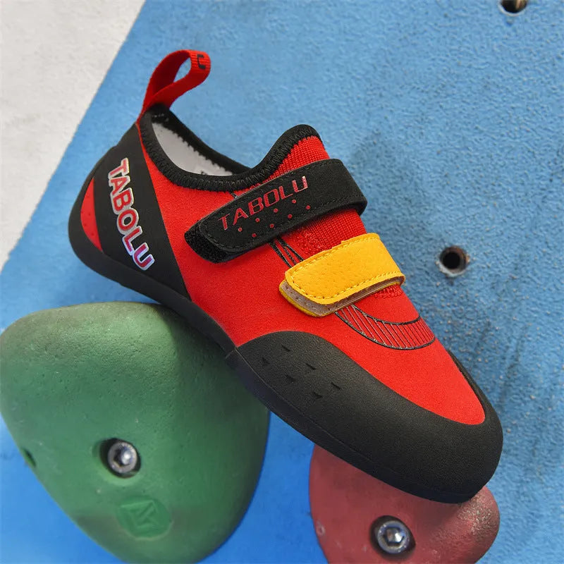 A pair of beginner rock climbing shoes with a velcro strap, shown in a black and red colour combination.