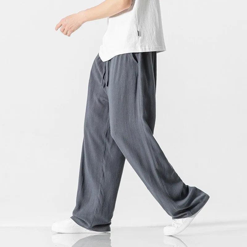 Men's beige loose straight-leg linen trousers with a drawstring waist on a neutral background.