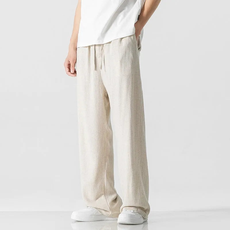 Men's beige loose straight-leg linen trousers with a drawstring waist on a neutral background.