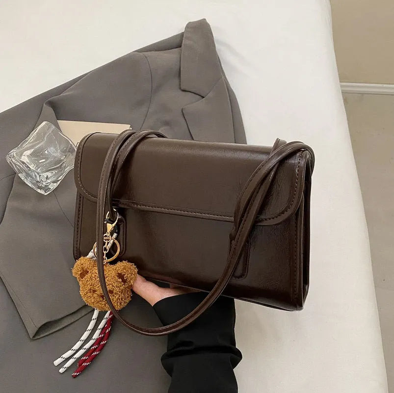Brown women's PU leather square shoulder bag with double straps and a matching tassel pendant on a table.