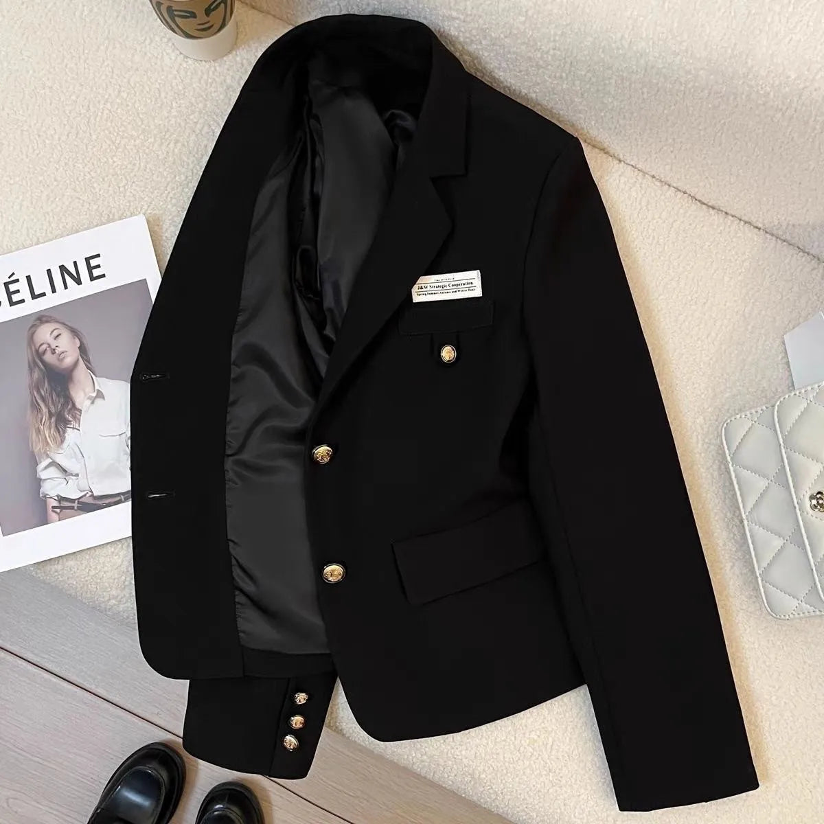 Women's black loose-fit short suit coat with long sleeves and pockets, shown on a hanger.