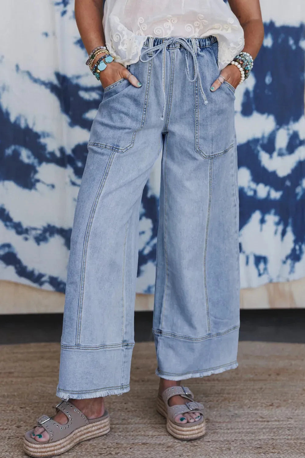 Beau Blue colour wide leg denim trousers with a drawstring waist and raw hem seam detail laid flat.