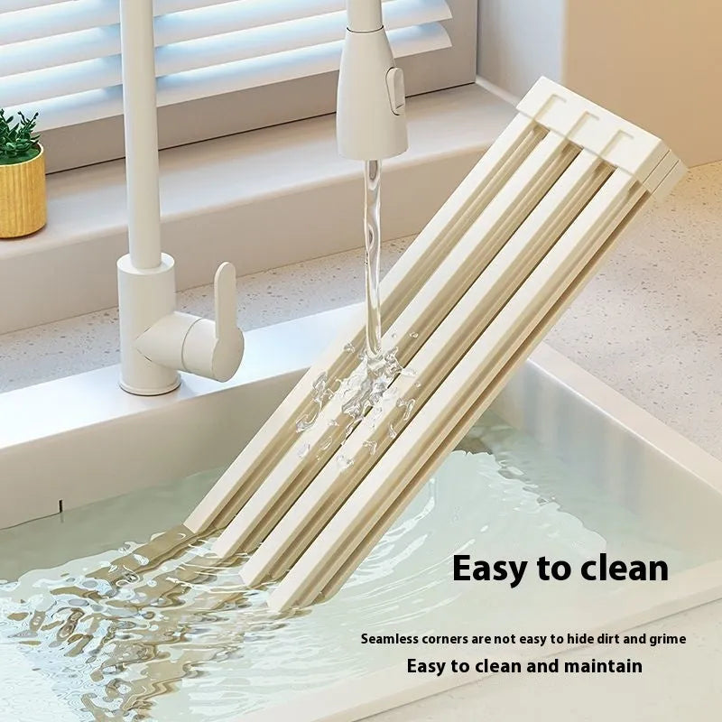 Milky white tri-fold stainless steel kitchen draining rack shown unfolded next to a sink.