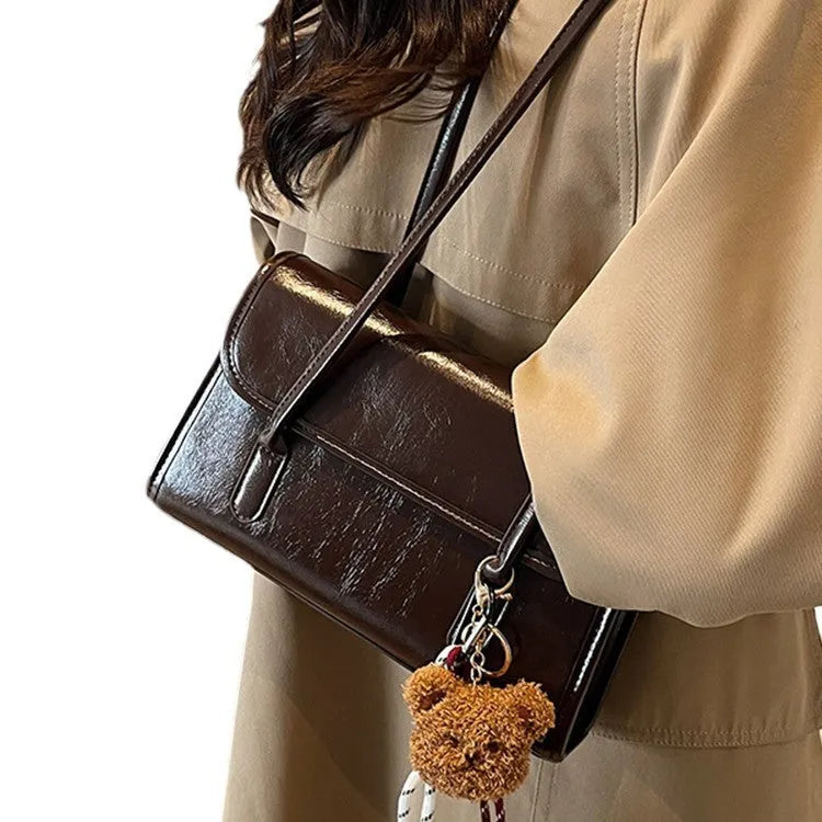 Brown women's PU leather square shoulder bag with double straps and a matching tassel pendant on a table.