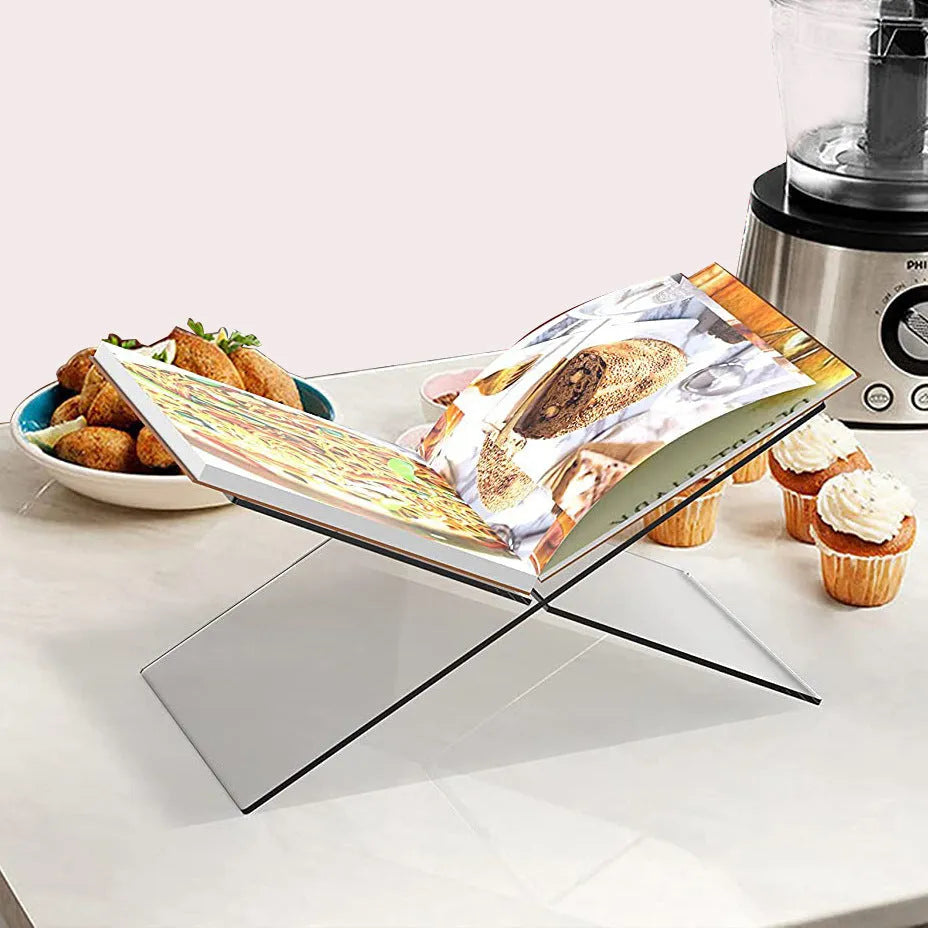 Clear acrylic X-shaped book reading rack holding an open book on a desk.