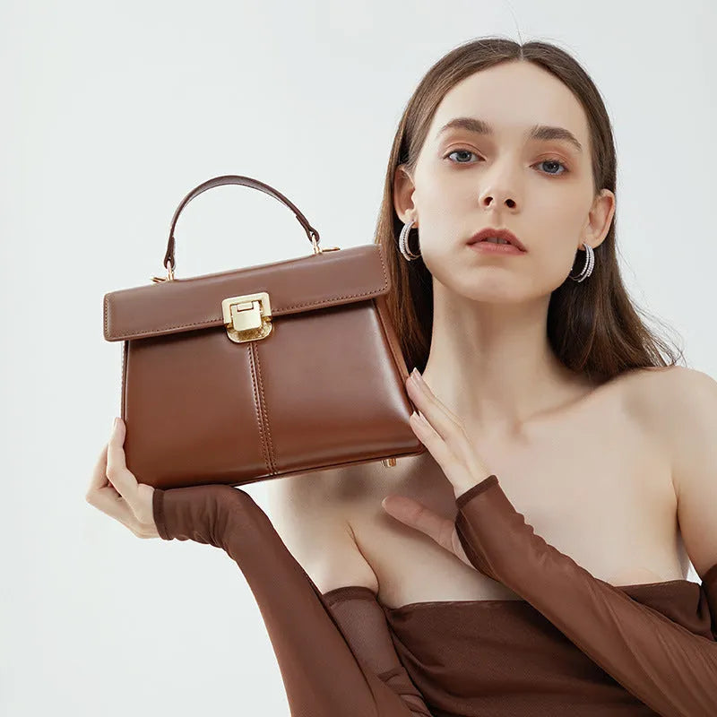 Black leather women's shoulder bag with vachette clasp showing square shape and adjustable strap.