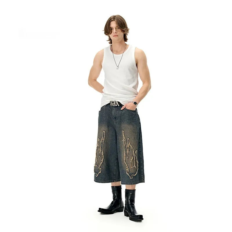 Men's black cropped denim shorts with red and orange patch flame embroidery on the leg.
