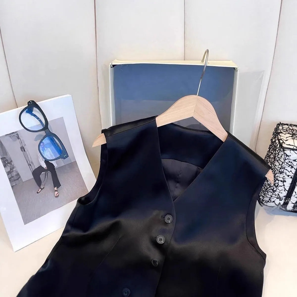 Black sleeveless satin vest for women on a hanger, showing loose fit and splicing detail.