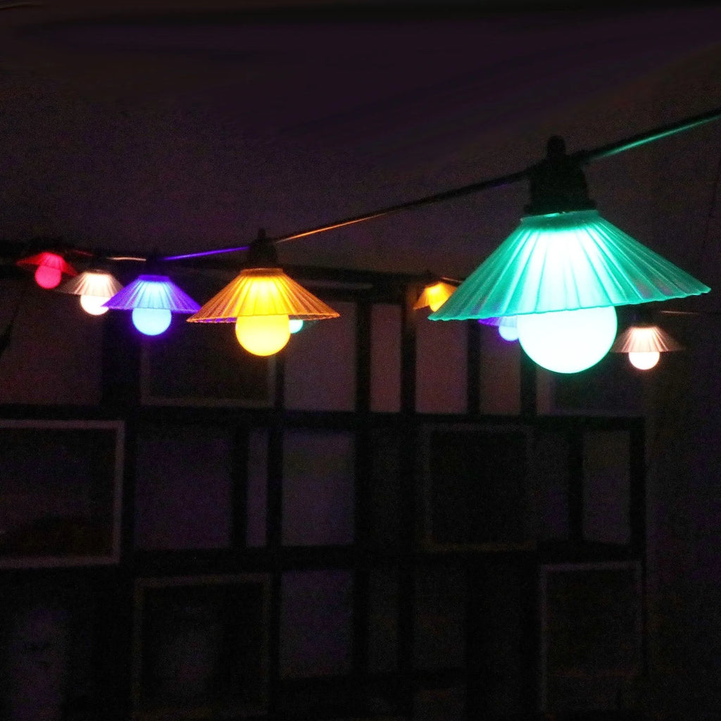 Outdoor LED string lights with flower-shaped globes in four colours, hanging in a garden.