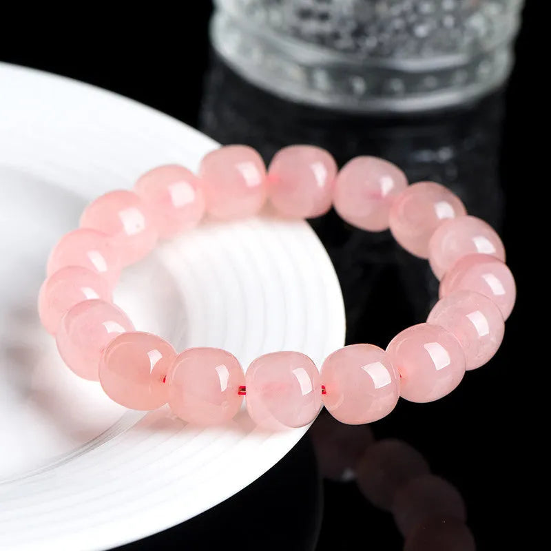 Pink natural crystal bracelet with polished geometric barrel-shaped beads on a wrist.