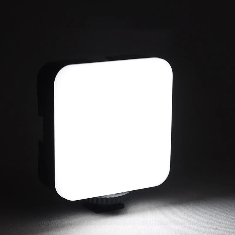 Square-shaped mini LED camera flash with hot shoe mount on a small tripod stand.
