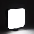 Square-shaped mini LED camera flash with hot shoe mount on a small tripod stand.