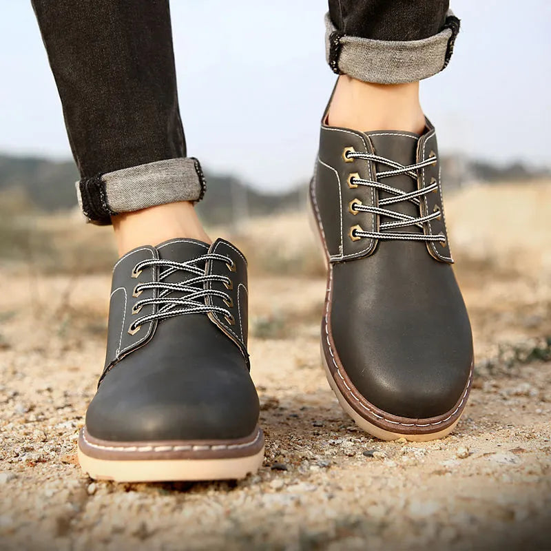 Men's black mid-top leather boots with a flat rubber sole shown from the side.