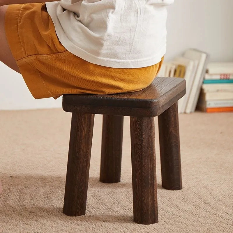 Solid wood distressed finish changing stool with bracket legs on a wooden floor.