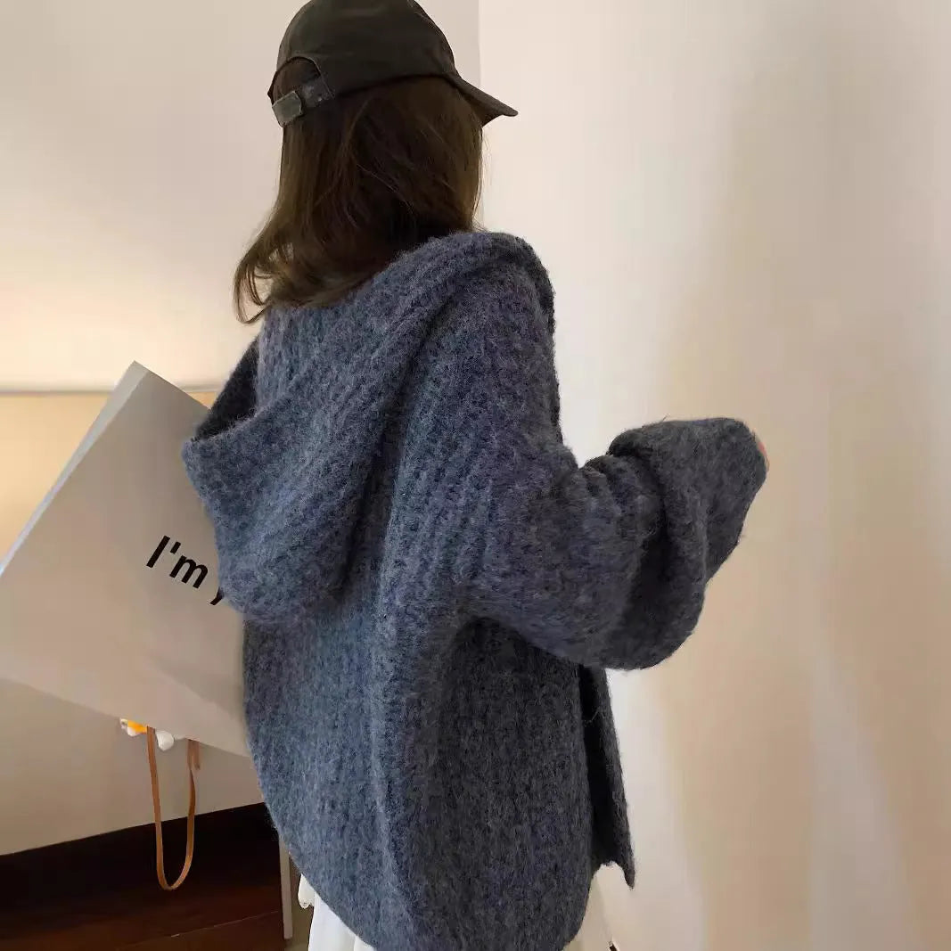 A woman wearing a thick, dark grey hooded cardigan with a loose fit and regular sleeves.