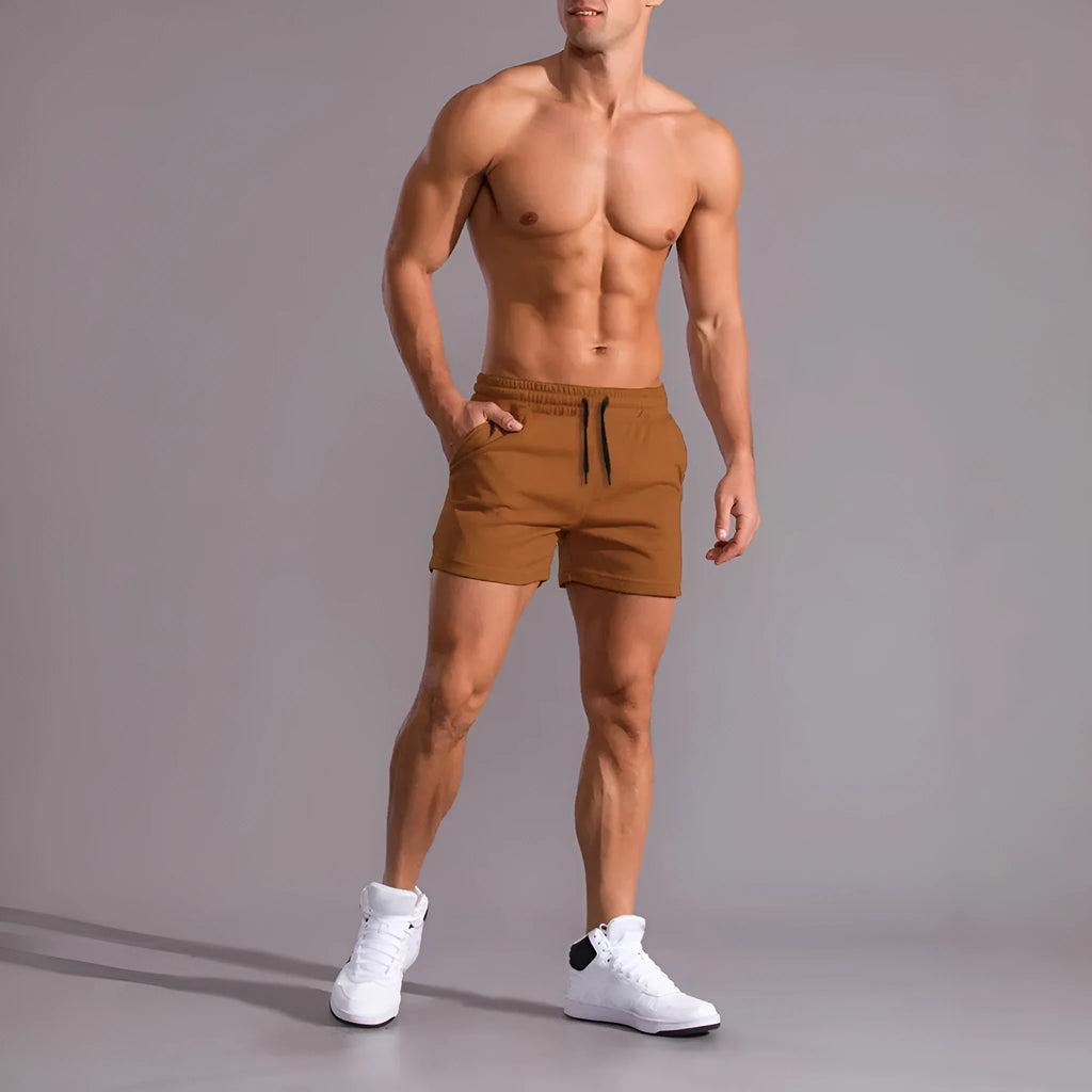Three men's drawstring shorts in black, khaki and light brown laid flat, showing elastic waistband and loose leg design.