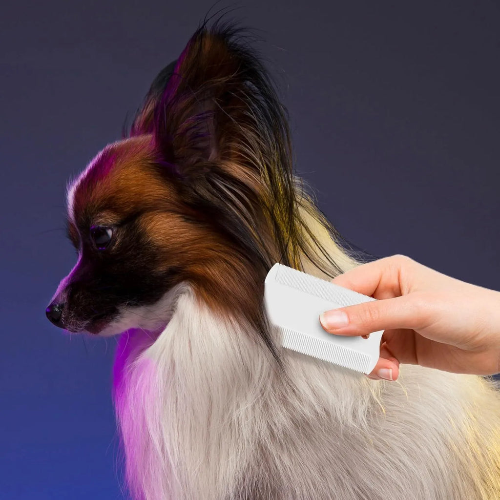 A small white plastic double-sided flea comb for pets, shown next to a ruler for scale.